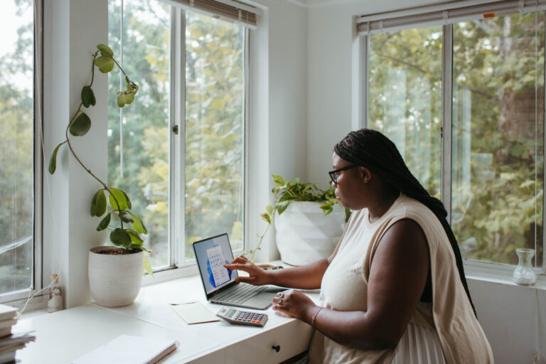Una mujer sentada en un escritorio y trabajando en un portatil con una calculadora