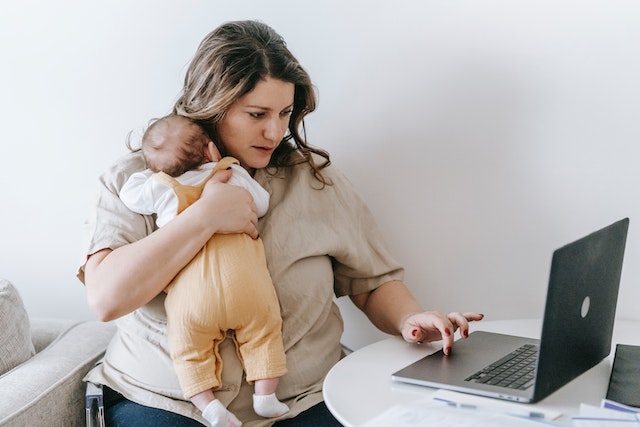 madre con su hijo en brazos usando un ordenador