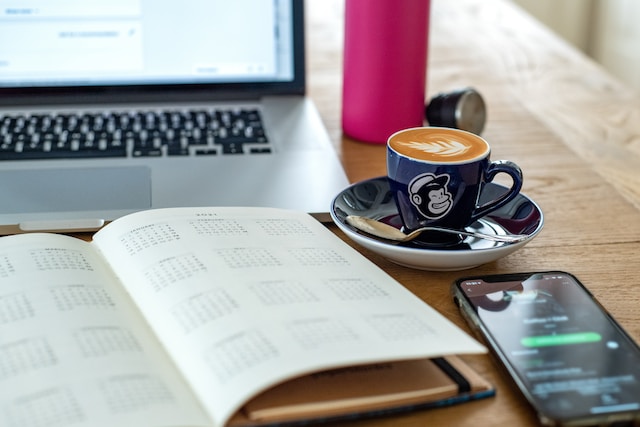 Agenda, ordenador, móvil y café encima de una mesa.