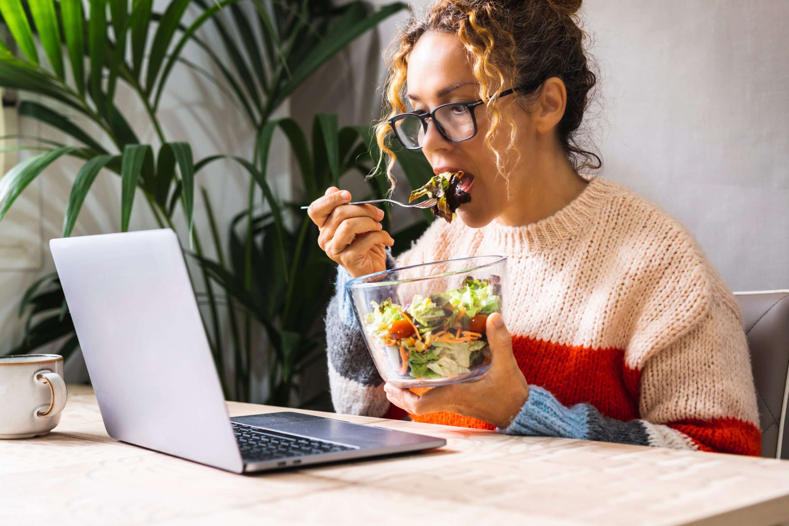 mujer comiendo ensalada enfrente de su ordenador mientras trabaja